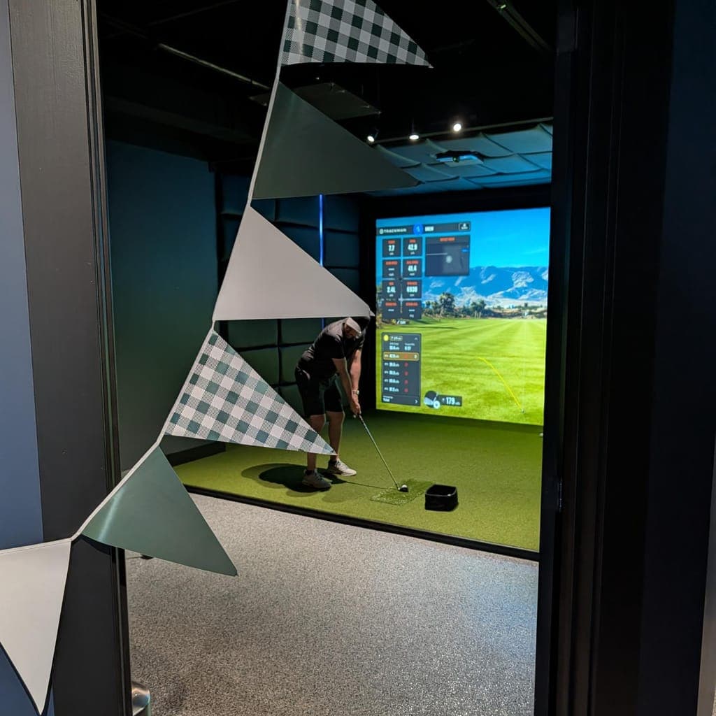 Golfer hitting a shot in a private bay decorated with party bunting at LevelUp Indoor Golf